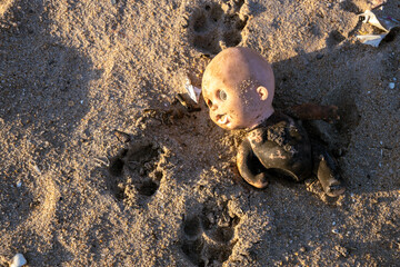 Old doll broken and abandoned on a beach. Plastic waste in nature.
