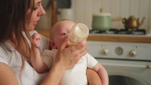 Happy family at home. Mother holding little baby toddler child feeding milk from bottle. Newborn Infant baby girl sucking eating drinking milk. Mom of breast feeding baby. Motherhood happy child