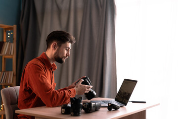 Professional photographer holding camera using laptop sitting at workplace. Concept of professional photography and creative career