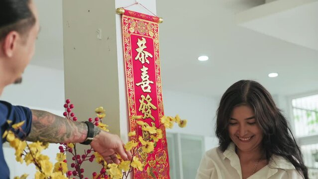 Asian family hanging scroll with calligraphy of good wishes and firecrackers on wall, decorating apricot blossoms with red lantern while preparing home for Tet celebration