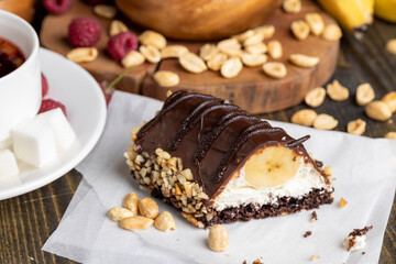 Sliced sweet cake with banana, chocolate glaze, milk filling and peanuts