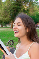 Obraz premium Beautiful young brownhair girl smells a fresh printed book sitting on the bench in the park