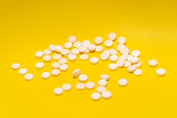 Several white color pills placed on top of a yellow surface.