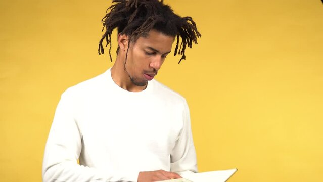 Young black male student in white sweater opens notebook and starts to wright