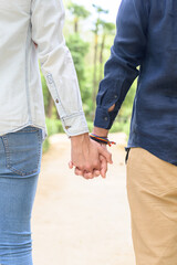 Crop unrecognizable gay couple holding hands while standing outdoors