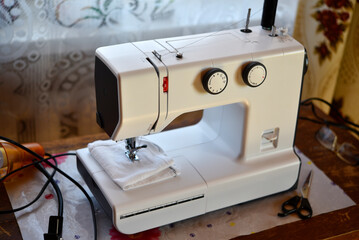 A white sewing machine in the room. Processing of clothes with a sewing machine.