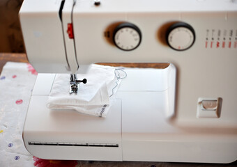 A white sewing machine in the room. Processing of clothes with a sewing machine.