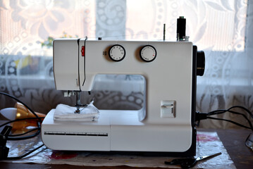 A white sewing machine in the room. Processing of clothes with a sewing machine.