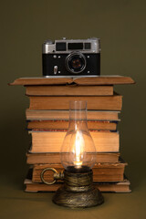 Old books, an old camera and a vintage style lamp with the light on.