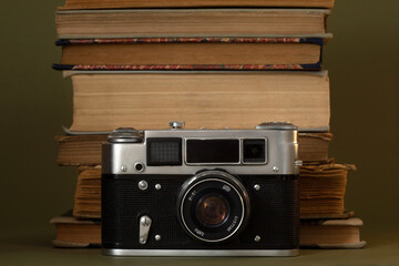 Old books stacked and an old camera on an olive green background.