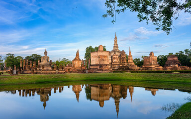 Fototapeta premium Beautiful wide view of ruins of Wat Mahathat Sukhothai at sun set with white clouds and blue sky on background. UNESCO and World Heritage Site. Travel Concept.