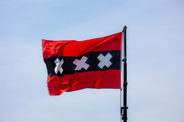 Official flag of Amsterdam waving on the air in a sunny day and blue sky background, The flag depicts three Saint Andrew's Crosses and is based on the escutcheon in the coat of arms of Amsterdam.