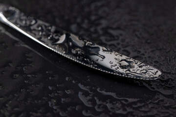 Fototapeta premium a steel knife covered with water droplets on black paper