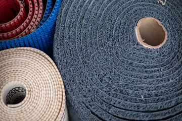 Fototapeta na wymiar Various mats in rolls for yoga, for bath, for entrance area, for shoes are on market for sale. Household goods.