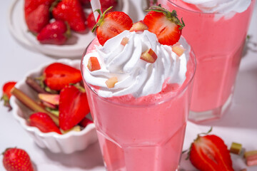 Rhubarb and strawberry milkshake or smoothie, refreshing summer drink, Healthy dieting and antioxidant summer beverage with whipped cream, fresh rhubarb, strawberry slices, on white kitchen table