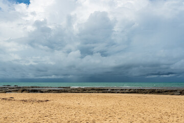 Fototapeta na wymiar Rainy sky above brazilian beach surrounded by rocky barrier 