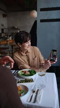 Handsome elderly woman shows photo on cell phone to her husband on date in cafe 