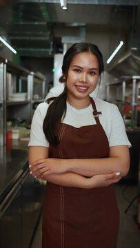 Happy asian business owner in apron looking at camera in cafe kitchen