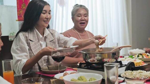 Young Asian woman sitting next to grandma and putting food into steaming hot pot while making traditional vietnamese dish for family on Tet holiday dinner at home