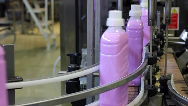 Bottles with Blue Liquid Moving Along Conveyor Belt in Cleaning Product Manufacturing Chemical Plant. A Conveyor Belt Carries Filled Bottles of Fabric Softener or Liquid Laundry Detergent.