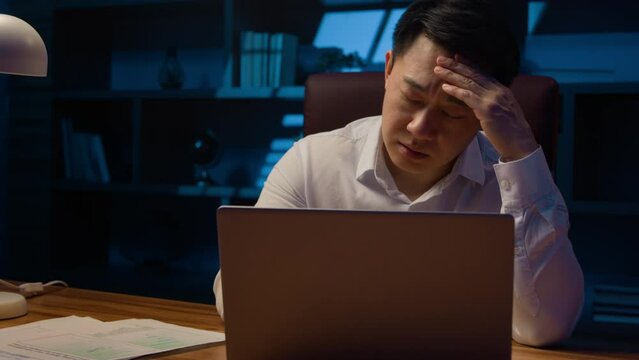Asian stressed tired Korean man middle-aged exhausted overworked businessman laptop working problem paperwork business trouble bad result documents failure difficulties stress at night evening office