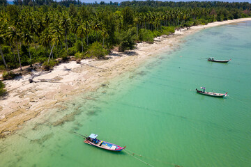 Traditional Thai Longtail fishing boats anchored off a small, palm tree lined tropical beach (Khao...