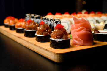 Closeup photo of maki rolls with salmon and tobiko calve on wooden serving board on dark upside