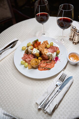 Plate with different snacks and red wine on white table in the restaurant