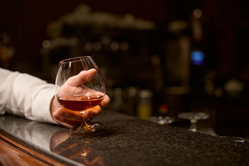 Male customer relaxing with glass of cognac at bar counter