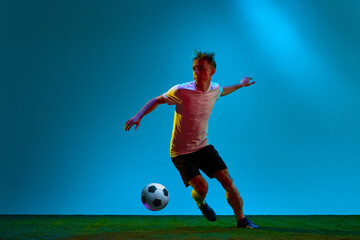 Obraz na płótnie Canvas One energetic guy, sportsman, soccer player wearing black and white uniform training on football field in neon light. Concept of action, energy, sport