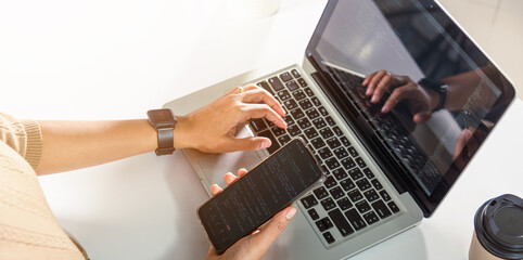 Programmer woman looking mobile phone program code at workplace, software developer hands typing data coding programming javascript with laptop computer, IT startup concept, Web application design