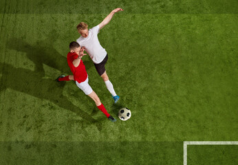 Two of football player in sportswear and football boots playing, training with ball over green grass field background. Aerial view