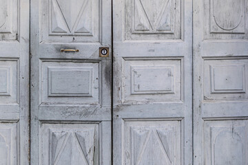 Old gray wooden entrance door with metal lock of an ancient Italian building in Via delle Orfane. Background of worn wooden door painted light blue-grey. Turin, Italy. 