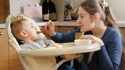 Portrait of mother playing with her baby son in airplanes while feeding him in highchair. Concept of parenting, healthy nutrition and baby care.