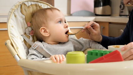 Portrait of happy smiling baby boy getting messy while eating in highchair. Concept of parenting, healthy nutrition and baby feeding.