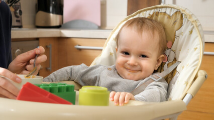 Portrait of cute smiling baby boy sitting in highchair after having breakfast and looking in camera