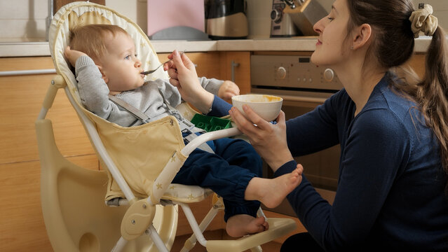 Little Baby Being Silly And Naughty While Eating Porridge In Highchair. Concept Of Parenting, Healthy Nutrition And Baby Feeding.