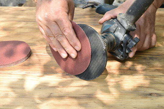 The man's hand is fixing a grinding wheel made of sandpaper on a special tool inserted into a drill.