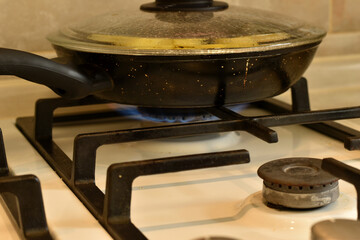 On a burning fire of a gas stove, food is heated in a frying pan.