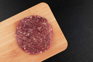 Raw hamburger patties on wooden cutting board on black background