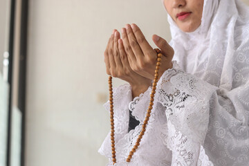 Asian Muslim woman wearing traditional hijab clothes with rosary beads, praying in the mosque. Muslim woman raising hand pray