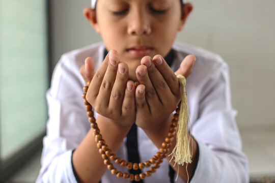 Close up of Asian Muslim kid praying while holding rosary prayer beads. Peace and love in the holy month of Ramadan. 