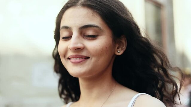 Charming young dark haired indian woman looking at the camera at the city street and enjoying beautiful day outdoors alone Pretty curly female at urban town at morning. High quality 4k footage
