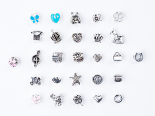 A variety of metal charms for a child's necklace or bracelet. Many charms isolated on a white background: star ,  flower,  lips, tree, cactus, lekki, etc. - obrazy, fototapety, plakaty