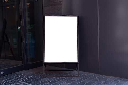 Blank white outdoor advertising stand/sandwich board mock up template. Clear street signage board placed by an outdoor dinning area of a restaurant. Background texture of standee on street.