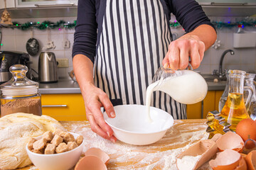 Woman pastry chef in a striped culinary apron pours milk while making homemade baking, close up.