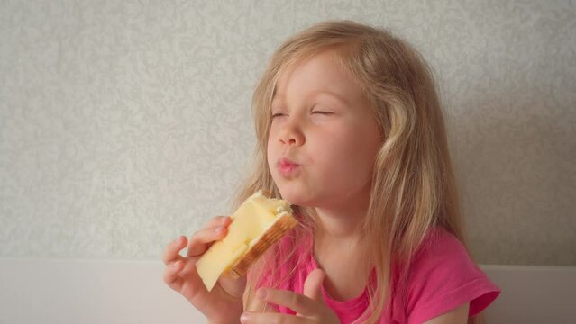 A cute little girl is eating a sandwich with cheese in bed. Close-up of beautiful blonde girl eating.