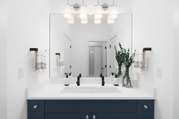 A bathroom with a blue cabinet, white marble countertop, cozy decorations. and black faucets.