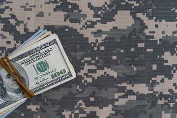 US dollar bills on fabric with texture of Ukrainian military pixeled camouflage. Cloth with camo pattern in grey, brown and green pixel shapes. Official uniform of Ukrainian soldiers close up.