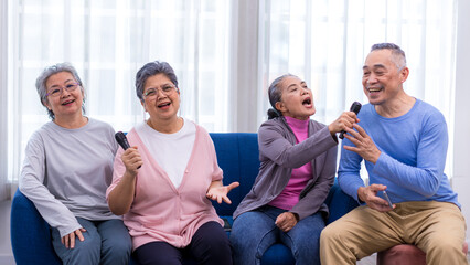 Happy senior Asian friends singing karaoke on the sofa in the living room with happy smiling face....